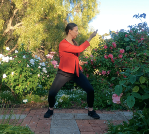 A woman surrounded by flowering plants practicing qigong in the park