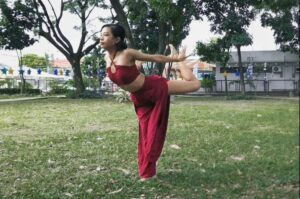 A woman wearing red outfit practicing crance qigong outside in the park on grass