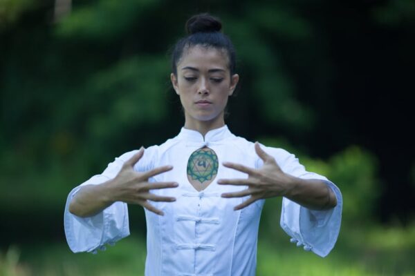 A woman practicing Zhan Zhuang outside surrounded by greeneries