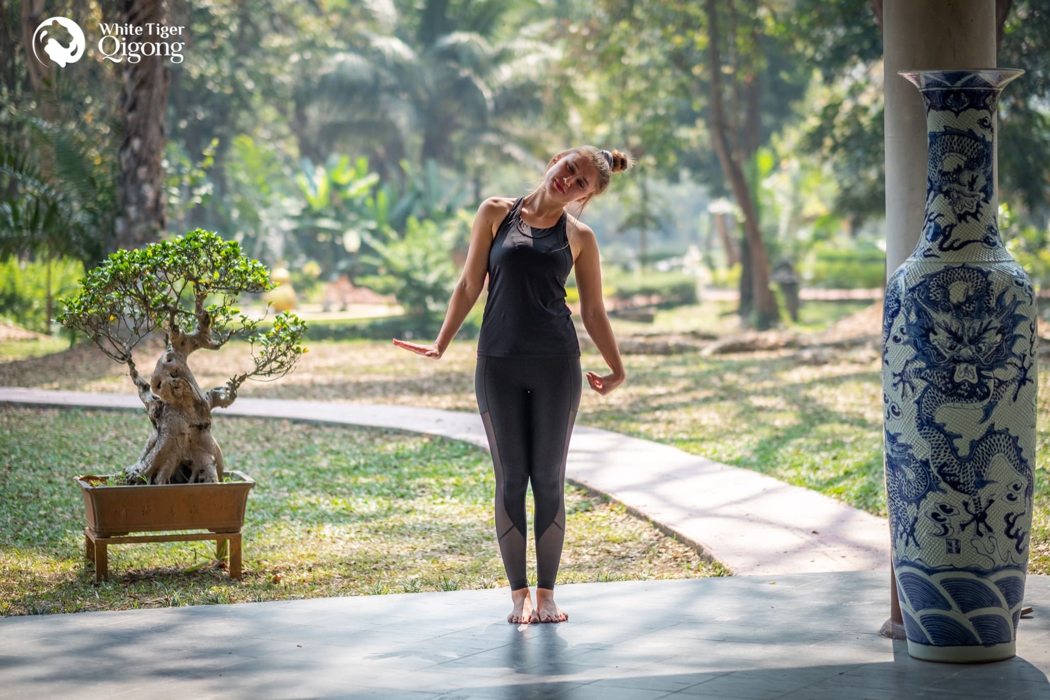 Qigong for Beginners - a woman in all black sporty outfit practicing qigong in the park surrounded by nature. 