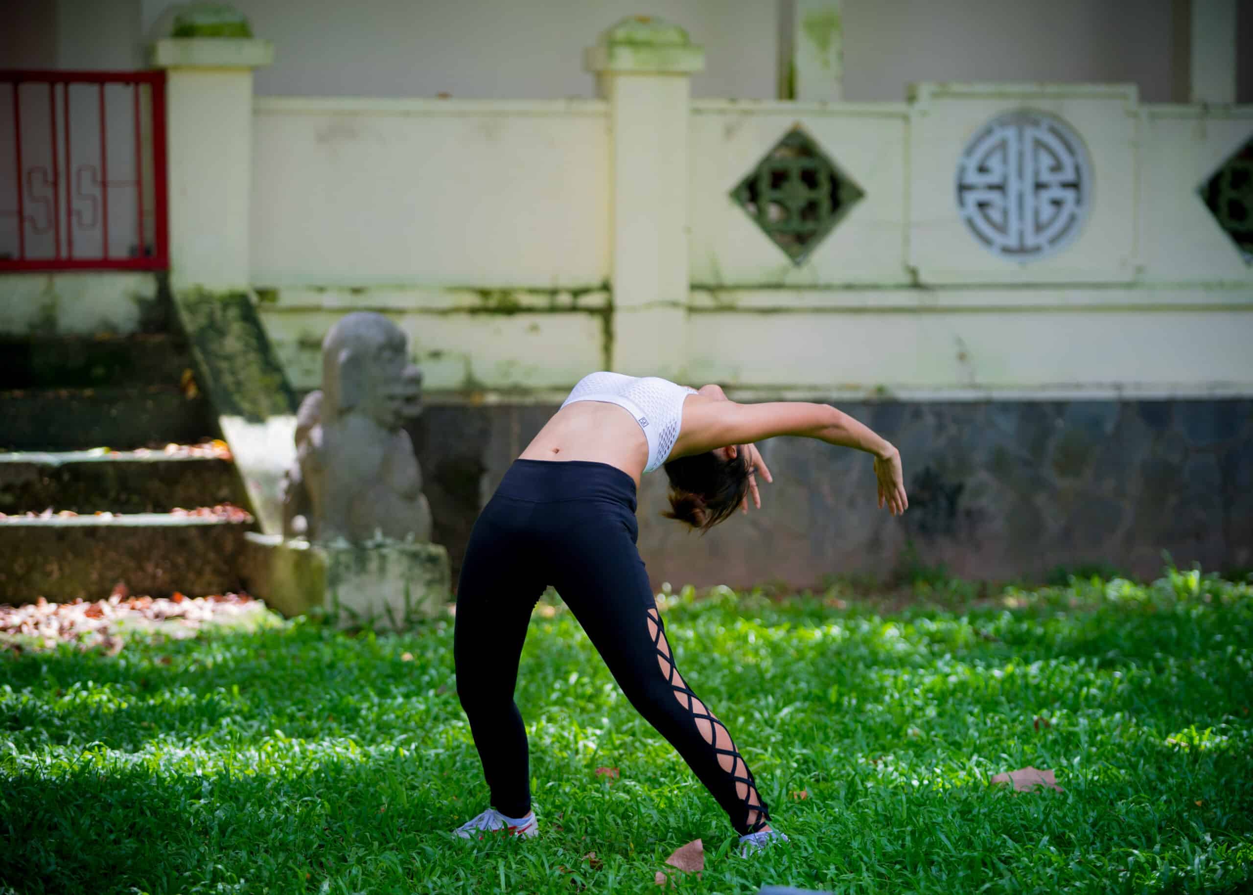 A woman in sports attire practicing qigong in the park surrounded by grass
